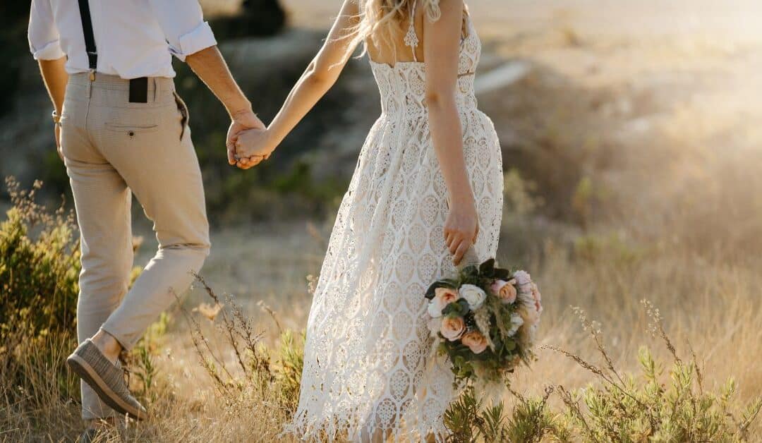 A wedding couple holding hands walking through a field